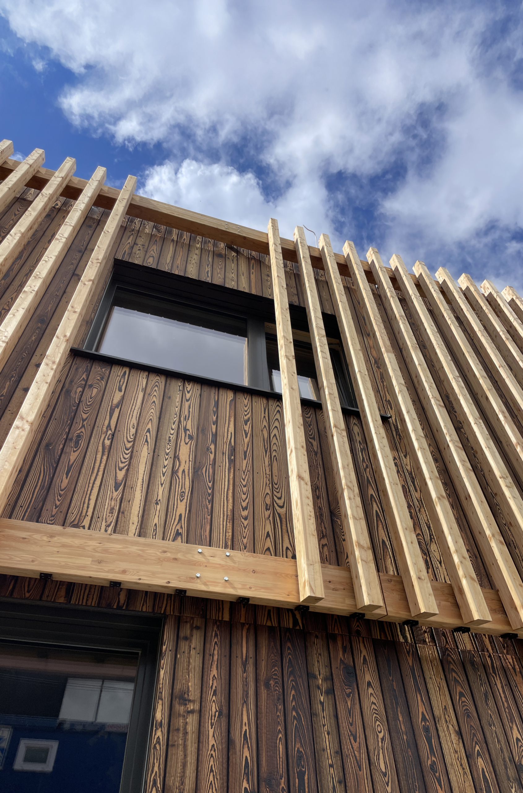 Houten gevel met geblakerde verticale planken en een horizontale balk met LamellenFix beugels en lamellen.